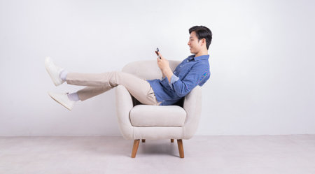 Young Asian man sitting on armchair on white backgroundの写真素材