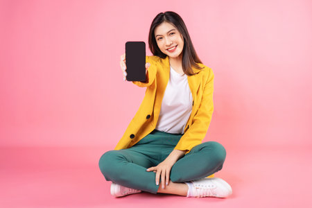 Image of young Asian businesswoman sitting and holding smartphone on backgroundの写真素材