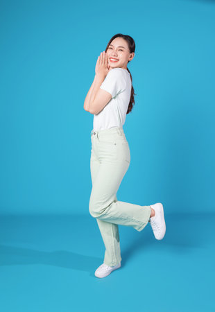 Full length photo of young Asian woman standing on blue backround