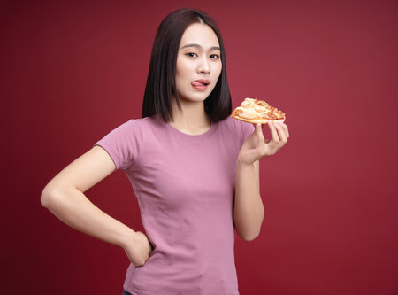 Young Asian woman eating pizza on backgroundの写真素材
