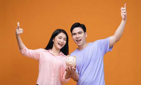 Young Asian couple holding piggy bank on backgroundの写真素材