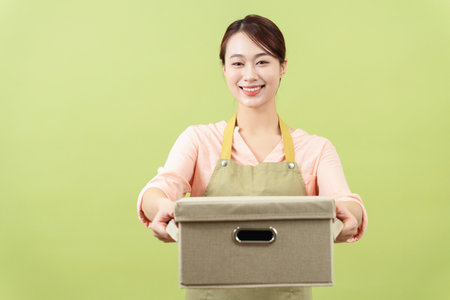 Photo of young Asian female housekeeper on green background