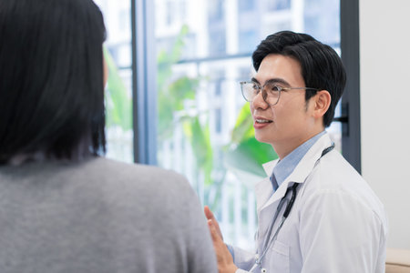 A healthcare professional engages in a conversation with a patient in a well-lit clinic. The doctor wears a lab coat with a stethoscope, discussing health concerns in a welcoming atmosphere.の写真素材