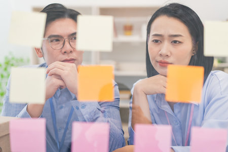 Two young professionals engage in a brainstorming session in a modern office. They observe colorful...