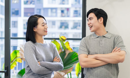 A man and woman engage in a cheerful conversation, standing with arms crossed in a contemporary office space adorned with lush plants.の写真素材