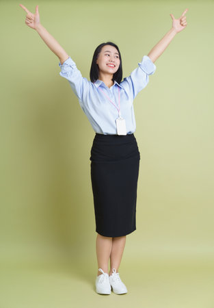 A young woman dressed in a light blue blouse and a black skirt stands confidently with her arms raised in a cheerful pose. The subtle green background enhances her bright demeanor.の写真素材