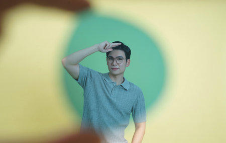 A young man, wearing glasses and a casual polo shirt, poses playfully. The backdrop features vibrant...