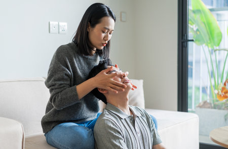 In a modern living room, a woman gently performs a facial treatment on a man, creating a soothing...