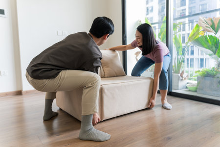 A young couple is working together to move a light-colored sofa in their modern apartment.の写真素材