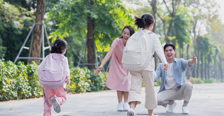 Two children happily run towards their parents in a lush park setting. The parents are beaming with joy, creating a warm atmosphere of family love and connection.の写真素材