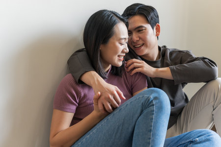 Two young adults share a joyful interaction while sitting together against a wall. Their expressions reveal happiness and affection, capturing a serene afternoon moment.の写真素材