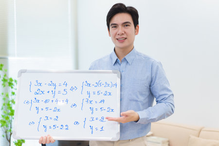 A young Asian male stands next to a whiteboard filled with math equations, explaining concepts to an unseen audience. The setting is bright and inviting, showcasing a home environment.の写真素材
