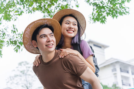 A young couple shares a lighthearted moment in a park, with the man giving a piggyback ride to the...