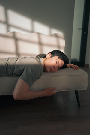 A person lies comfortably on a beige couch, basking in warm sunlight that filters through the window, creating a serene and peaceful ambiance in a stylish living room.の写真素材