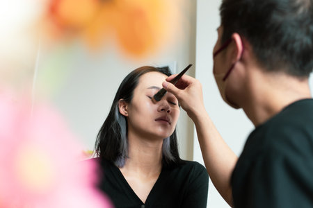 A skilled artist focuses on enhancing a model's features with makeup in a well-lit studio, showcasing a blend of artistry and professionalism. This informative session emphasizes beauty techniques.の写真素材