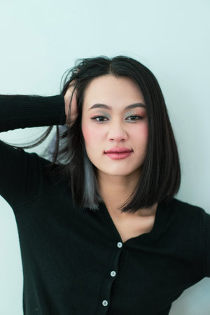 A young Asian woman poses confidently with her hand in her hair, showcasing her stylish bob cut. The light background highlights her features and relaxed expression.の写真素材