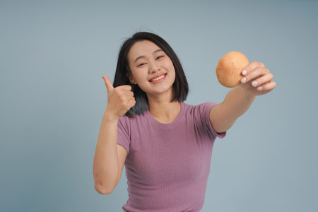 A cheerful young woman with short black hair holds up a soft bun with one hand while giving a thumbs...