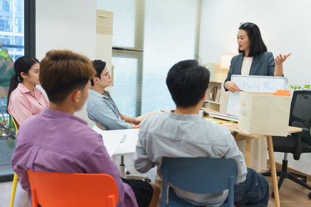 A group of four young professionals sit around a table in a bright office, listening intently as a...