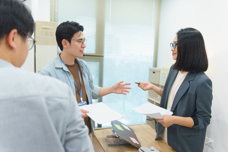 Professionals engage in a creative discussion in a modern office, sharing ideas using documents and notes. The atmosphere is vibrant, promoting teamwork and innovative thinking.の写真素材