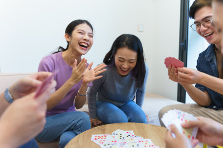 A lively group of friends is gathered indoors, sharing a joyful moment as they play cards. Their laughter highlights the camaraderie and fun atmosphere in the room.の写真素材
