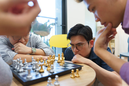 Four individuals concentrate intensely on a chessboard, surrounded by a modern interior. The...
