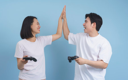 Two friends are enjoying their time playing video games, sharing a joyful moment as they high-five each other. They are in a bright room with a light blue background.の写真素材
