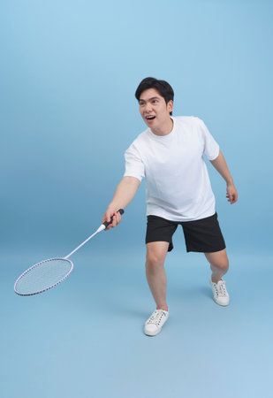 A young man is engaged in a badminton practice session indoors, demonstrating his skills with a racket. He is wearing a casual outfit and showing determination.の写真素材