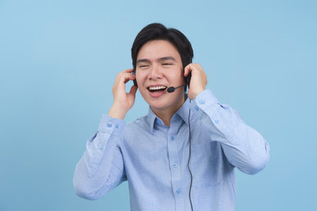 A young Asian man with a cheerful expression listens to music through headphones. He appears relaxed and happy, enjoying the sounds as he interacts playfully.の写真素材