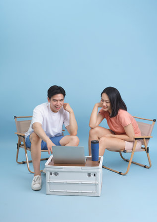 Two young adults sit in portable chairs, focused on a laptop placed on a cooler. The cheerful atmosphere reflects their enjoyment and engagement with technology.の写真素材