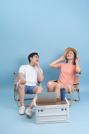 Two friends relax in outdoor chairs, sharing laughs under a bright blue sky. They are equipped with a laptop and drinks, embodying a carefree summer vibe.の写真素材