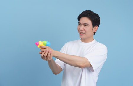 A man with dark hair is aiming a brightly colored water gun while smiling. He wears a simple white t-shirt, embodying a carefree spirit of summer playfulness and fun.の写真素材