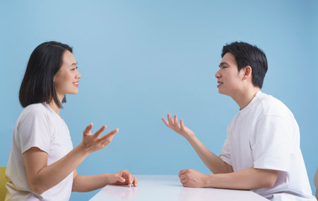 Two individuals are animatedly discussing at a white table, appearing relaxed and enjoying each...