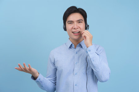 A young Asian man with a friendly expression is speaking into a headset while gesturing with his hand.の写真素材