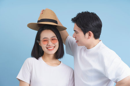 A young couple shares a lighthearted moment as the male places a straw hat atop the female's head. Both wear casual clothing and bright smiles, embracing the fun atmosphere.の写真素材