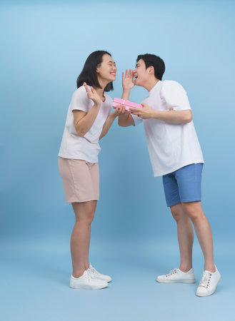 A happy young couple stands close together, exchanging playful whispers and laughter. They are dressed casually in light clothing, creating a cheerful atmosphere.の写真素材