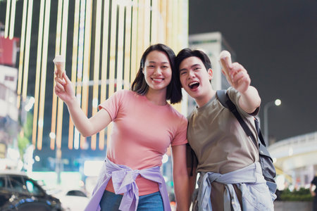 A cheerful couple stands on a bustling street in Hanoi, Vietnam, happily holding ice cream cones....
