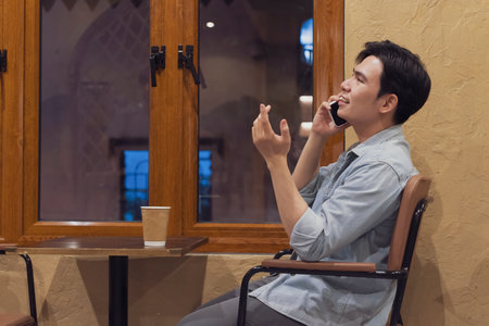 A man is sitting in a cafe in Hanoi, Vietnam, talking on the phone with a relaxed demeanor. The warm...