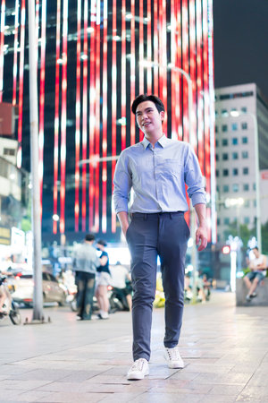 A young Asian man strolls through a vibrant street in Hanoi at night, illuminated by dynamic red and white lights. The hustle of the city surrounds him, creating an energetic atmosphere.の写真素材