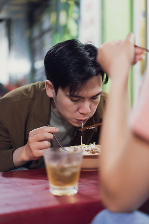 A young man enjoys his meal at a bustling street food stall in Hanoi, Vietnam.
