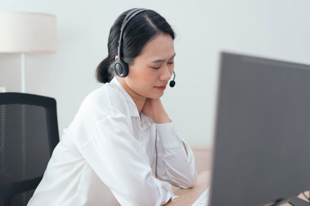 A woman with long hair pulled back sits at a desk wearing a headset, focused on her computer screen....
