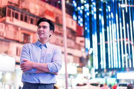 A young man stands with arms crossed, smiling amidst the lively nightlife of Hanoi. Bright neon lights illuminate the urban landscape, creating an energetic atmosphere in the city.の写真素材