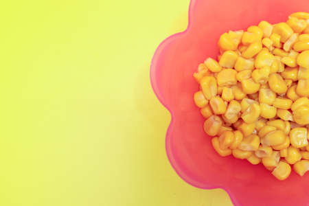 corn kernels in the pink bowl isolated on a yellow backgroundの写真素材