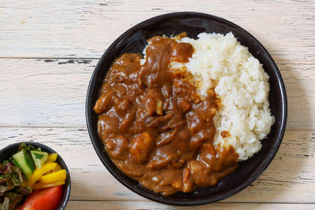Curry and rice to serve on a black plate on the wooden table.の写真素材