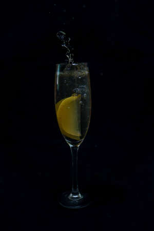 A glass of carbonated drink and a lemon in a black background.