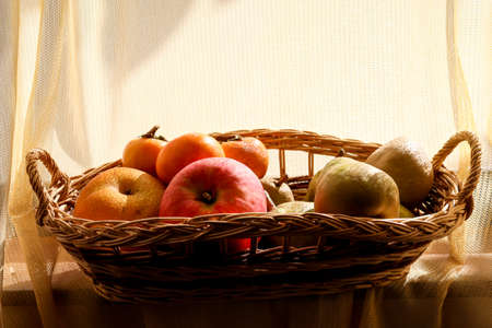Various kind of autumn fruits in the basket on the windowsill.