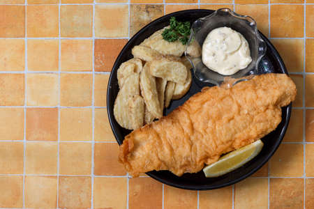 Fish and chips on the black dish isolated on a tile pattern background.