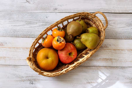 Various kind of autumn fruits in the basket on the wooden table.