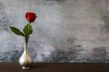 A red rose in the pewter vase put on the wooden table.の写真素材