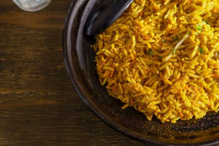 Curry-flavored fried rice on a black dish on a wooden table.