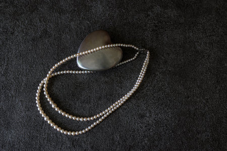 Pearl necklace and heart shaped metal object isolated on stone pattern board.の写真素材
